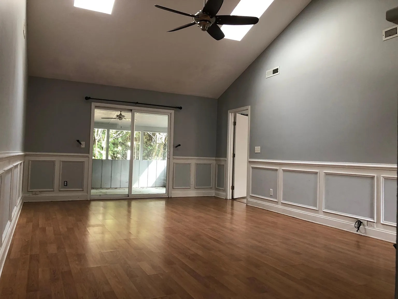 Living room before renovation: empty vaulted room with gray walls and dated wainscoting