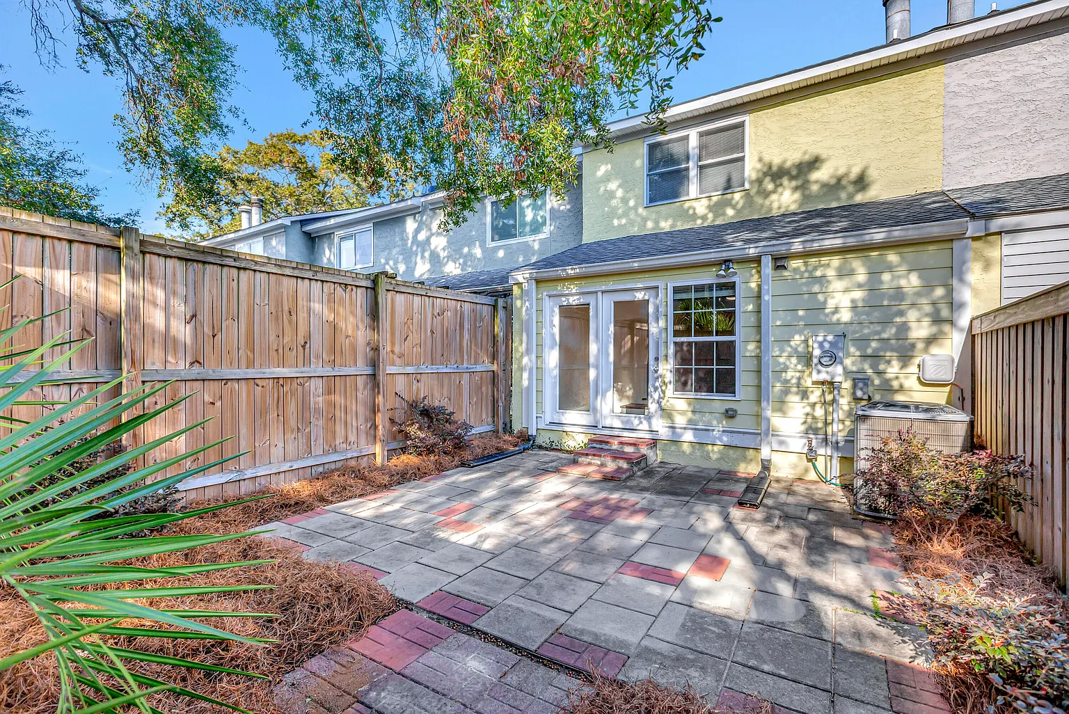 Backyard patio before renovation: dated pavers, bare fence, overgrown landscaping